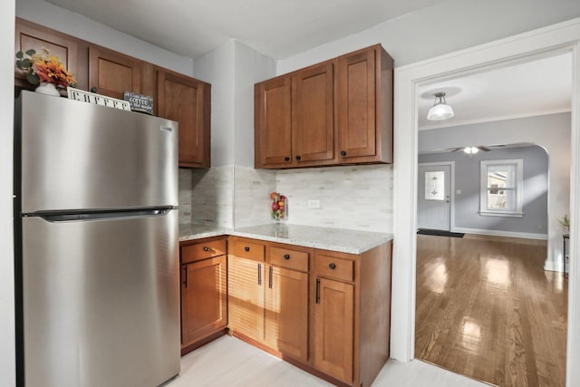 kitchen featuring light stone counters, tasteful backsplash, stainless steel refrigerator, ceiling fan, and light hardwood / wood-style floors