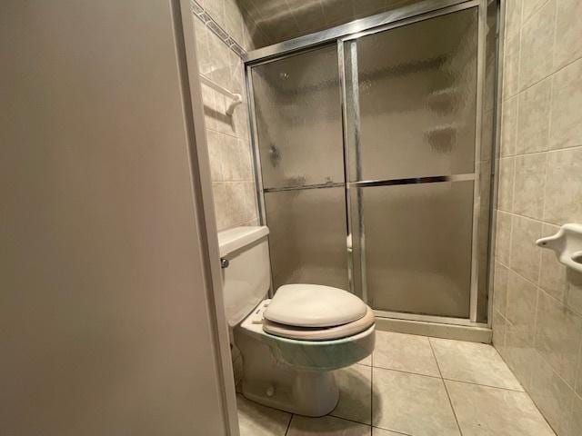 bathroom with toilet, a shower with door, tile patterned flooring, and tile walls