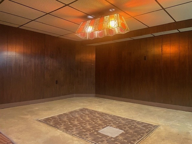 unfurnished room with a drop ceiling and wood walls