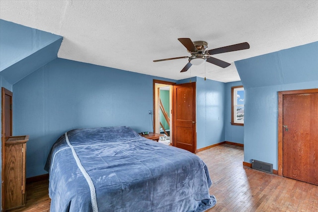 bedroom featuring ceiling fan, lofted ceiling, hardwood / wood-style floors, and a textured ceiling