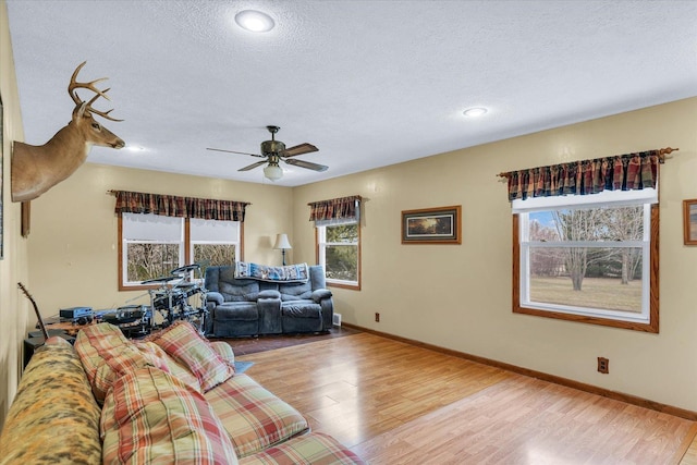 living room with ceiling fan, a textured ceiling, and light wood-type flooring