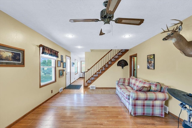 living room with ceiling fan, a textured ceiling, and light wood-type flooring