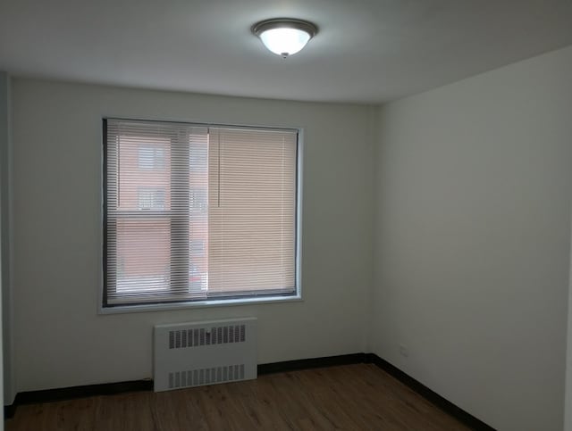 empty room with dark wood-type flooring and radiator