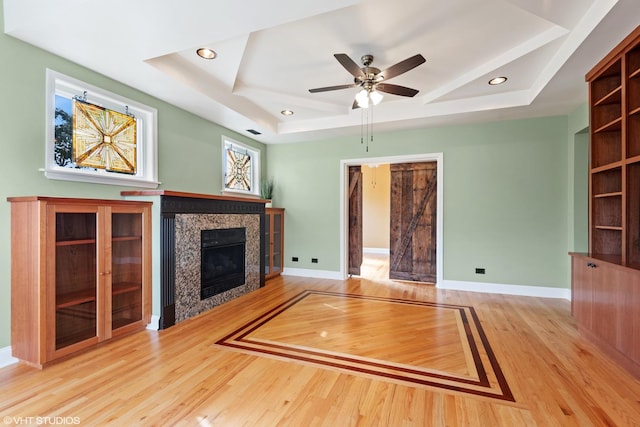 unfurnished living room featuring a tray ceiling, a tile fireplace, ceiling fan, and light wood-type flooring