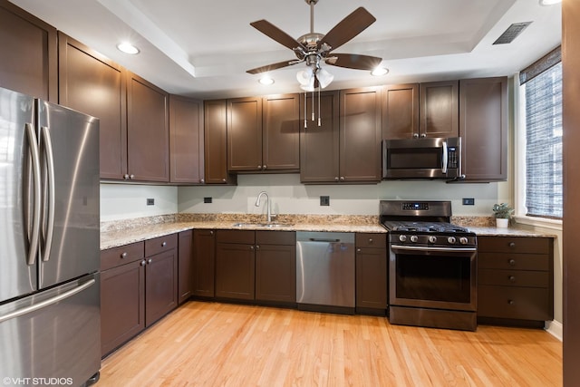 kitchen with a raised ceiling, appliances with stainless steel finishes, sink, and light hardwood / wood-style floors