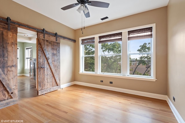 spare room featuring ceiling fan, a barn door, and light hardwood / wood-style floors