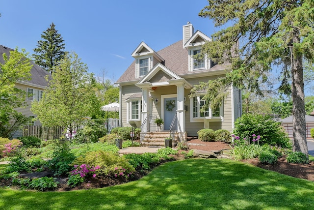 view of front of house with a front yard, roof with shingles, fence, and a chimney