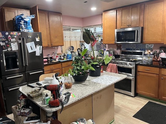 kitchen featuring light stone countertops, appliances with stainless steel finishes, backsplash, and light wood-type flooring