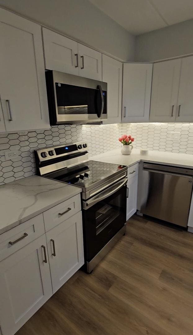 kitchen featuring white cabinetry, appliances with stainless steel finishes, dark hardwood / wood-style floors, and light stone counters