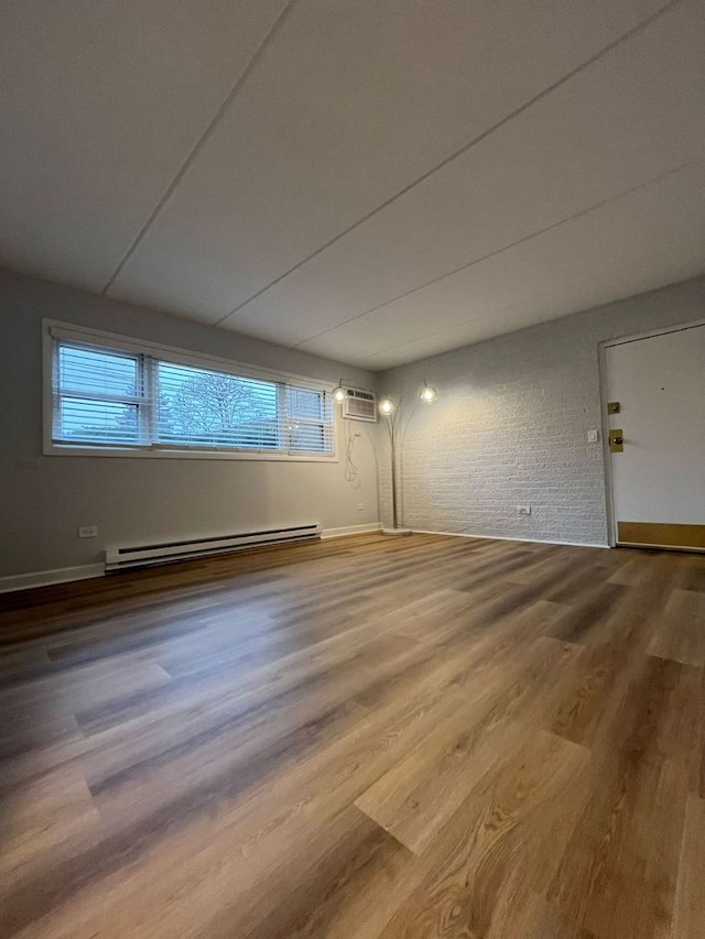 spare room with a baseboard radiator, an AC wall unit, wood-type flooring, and brick wall