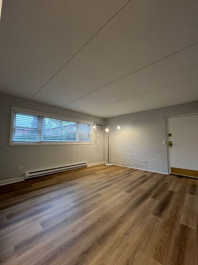 unfurnished room featuring wood-type flooring, a wall unit AC, brick wall, and baseboard heating