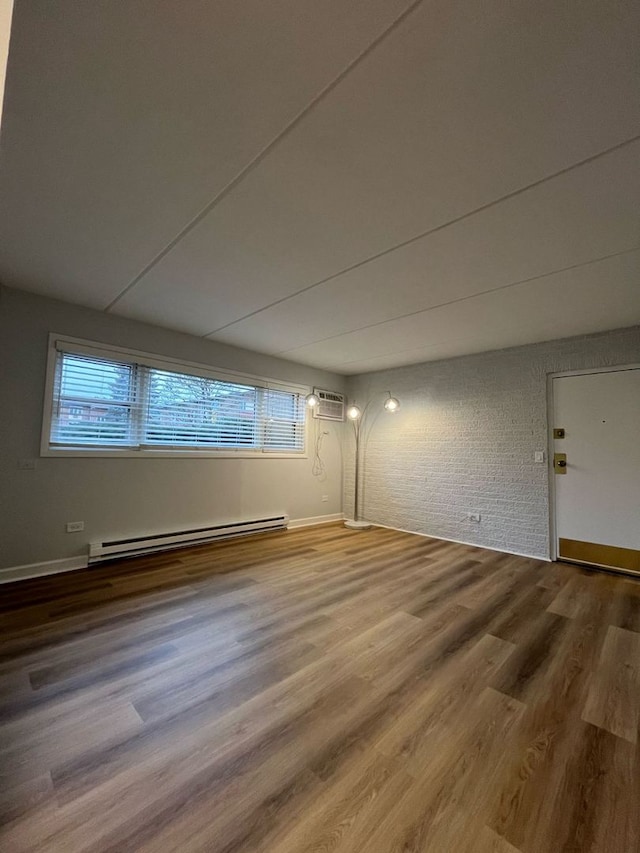 unfurnished room with a baseboard heating unit, wood-type flooring, an AC wall unit, and brick wall