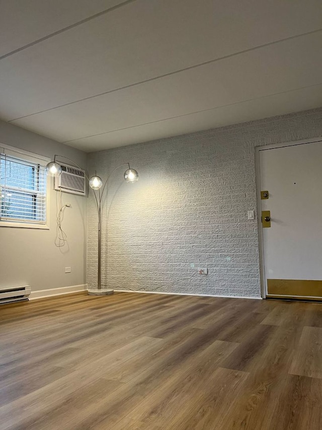 unfurnished room with hardwood / wood-style floors, an AC wall unit, and brick wall