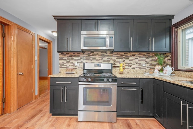 kitchen featuring appliances with stainless steel finishes, light stone countertops, light hardwood / wood-style flooring, and backsplash