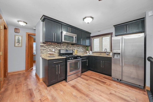 kitchen featuring sink, light wood-type flooring, appliances with stainless steel finishes, light stone countertops, and backsplash