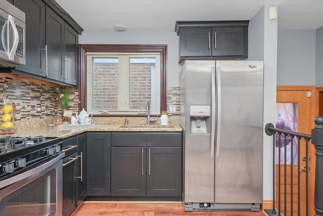 kitchen featuring sink, tasteful backsplash, light hardwood / wood-style flooring, stainless steel appliances, and light stone countertops