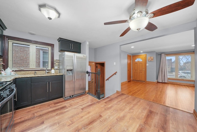 kitchen with sink, light stone counters, gas range oven, stainless steel refrigerator with ice dispenser, and light wood-type flooring