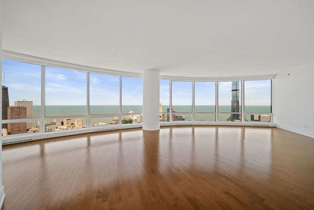 empty room with floor to ceiling windows, a water view, baseboards, and hardwood / wood-style flooring