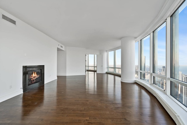 unfurnished living room featuring a glass covered fireplace, baseboards, dark wood-type flooring, and visible vents