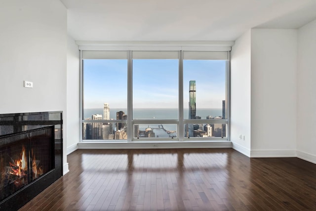 unfurnished living room with a water view, floor to ceiling windows, dark hardwood / wood-style flooring, and plenty of natural light