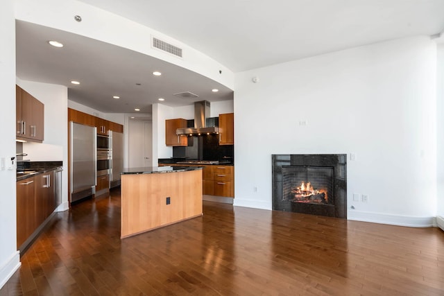 kitchen featuring wall chimney range hood, dark countertops, dark wood-style floors, and a center island
