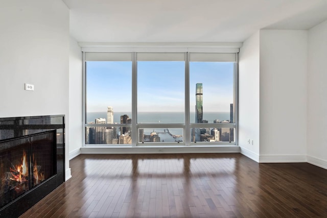 living room featuring baseboards, expansive windows, a lit fireplace, and hardwood / wood-style flooring