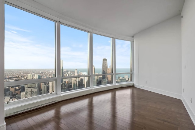 unfurnished room featuring a city view, dark wood-style flooring, and baseboards