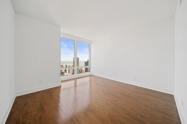 empty room with baseboards, dark wood-style flooring, visible vents, and floor to ceiling windows