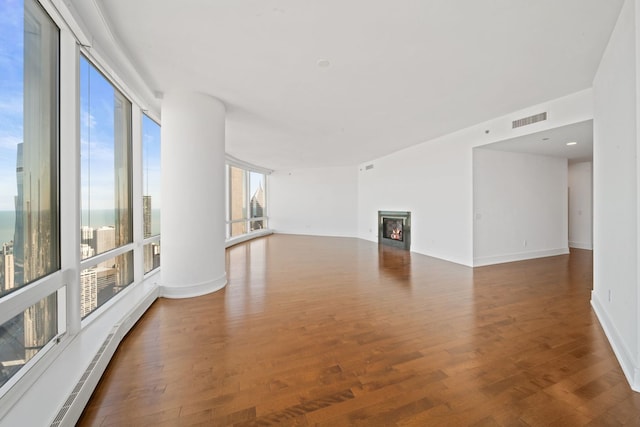 unfurnished living room featuring baseboard heating, baseboards, visible vents, a lit fireplace, and wood finished floors