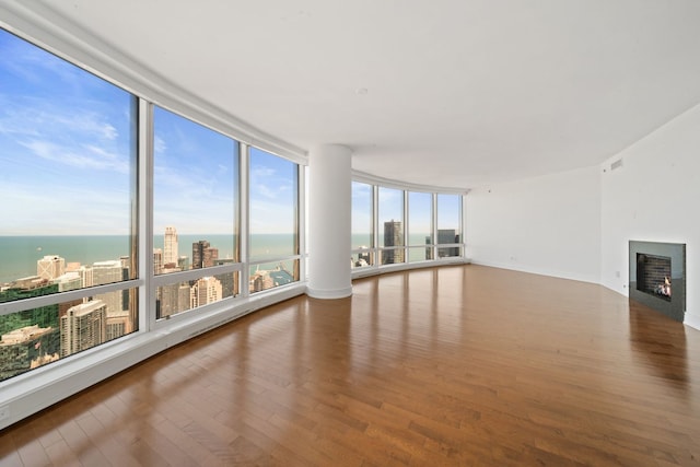 unfurnished living room featuring baseboards, visible vents, a water view, a lit fireplace, and wood finished floors