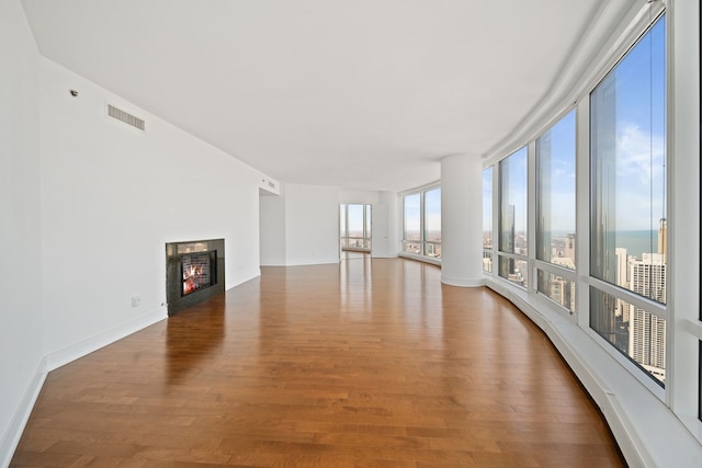unfurnished living room with baseboards, visible vents, a lit fireplace, and wood finished floors