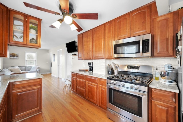 kitchen featuring light hardwood / wood-style flooring, ceiling fan, appliances with stainless steel finishes, backsplash, and light stone countertops