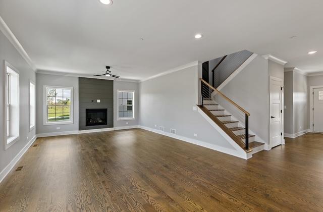 unfurnished living room with hardwood / wood-style flooring, ornamental molding, ceiling fan, and a fireplace