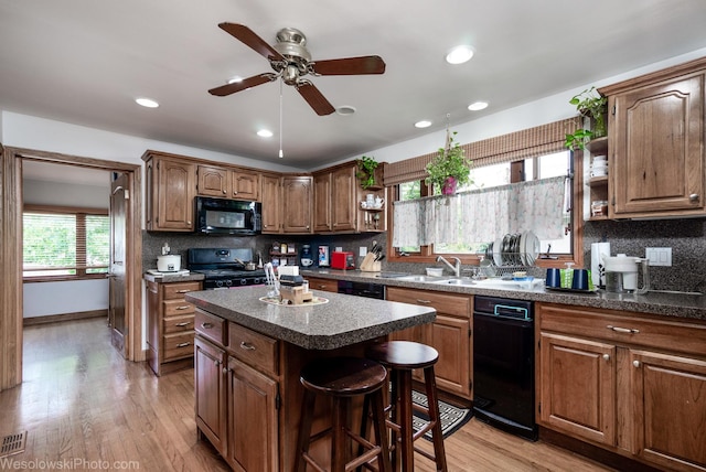 kitchen with light hardwood / wood-style flooring, a center island, sink, and black appliances