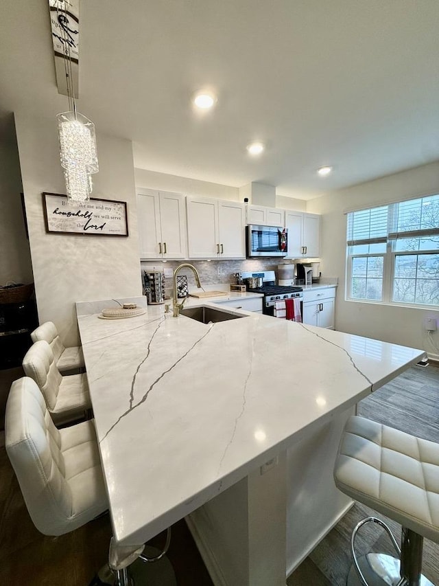 kitchen with white cabinetry, appliances with stainless steel finishes, a kitchen breakfast bar, and pendant lighting