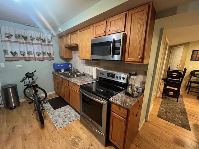 kitchen featuring sink, stainless steel appliances, tasteful backsplash, light hardwood / wood-style floors, and dark stone counters