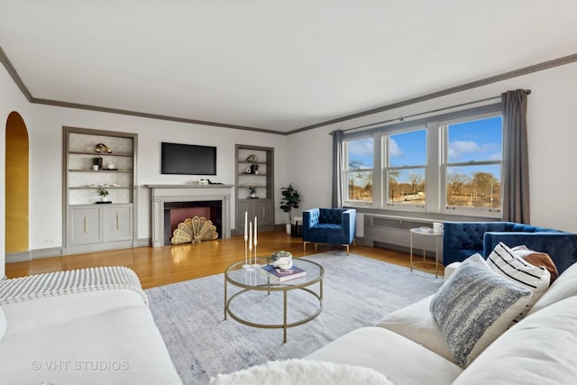 living room featuring wood-type flooring, ornamental molding, and built in shelves