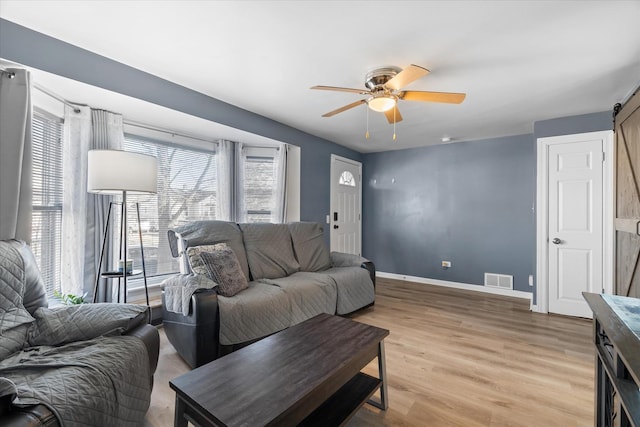 living room featuring light hardwood / wood-style floors, a barn door, and ceiling fan