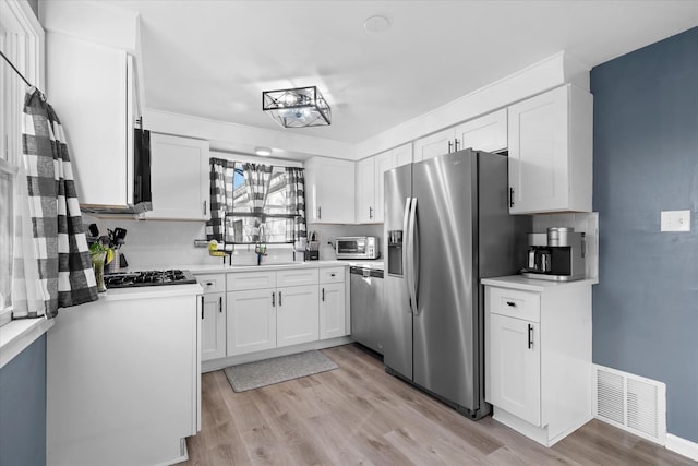 kitchen with sink, light hardwood / wood-style flooring, stainless steel appliances, white cabinets, and decorative backsplash