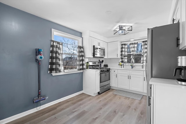 kitchen featuring appliances with stainless steel finishes, sink, white cabinets, and light hardwood / wood-style flooring