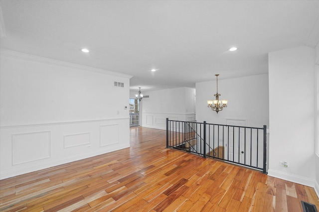 empty room featuring a notable chandelier, crown molding, and light hardwood / wood-style floors