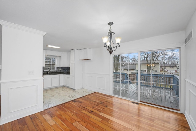 unfurnished dining area with sink, an inviting chandelier, and light hardwood / wood-style floors