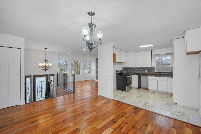 kitchen with stainless steel electric range, white cabinetry, tasteful backsplash, decorative light fixtures, and a chandelier