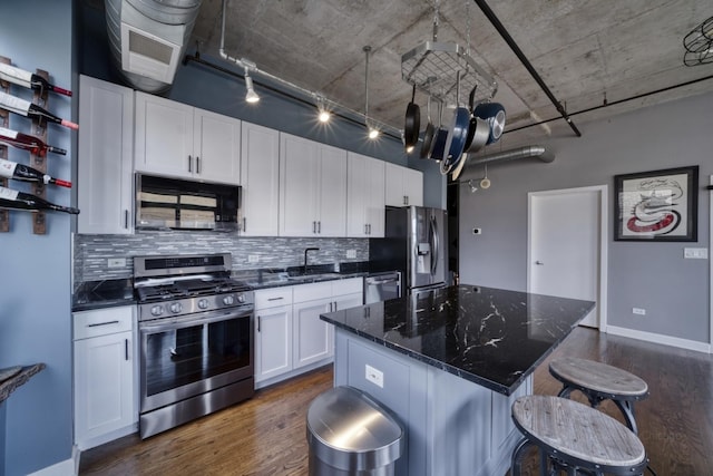 kitchen with a center island, dark stone countertops, dark hardwood / wood-style floors, stainless steel appliances, and white cabinets