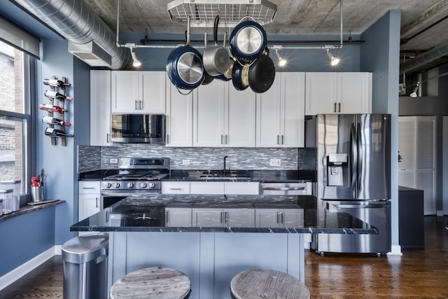 kitchen with white cabinetry, dark stone countertops, appliances with stainless steel finishes, and a breakfast bar area