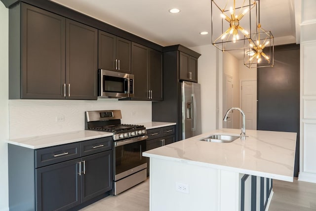 kitchen featuring pendant lighting, sink, appliances with stainless steel finishes, a kitchen island with sink, and light stone counters