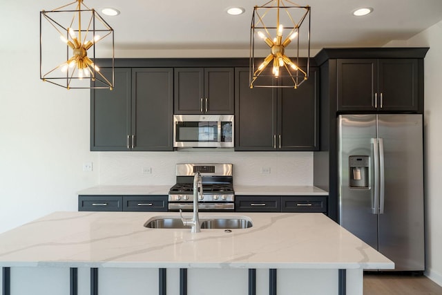 kitchen featuring stainless steel appliances, a kitchen island with sink, light stone counters, and decorative light fixtures