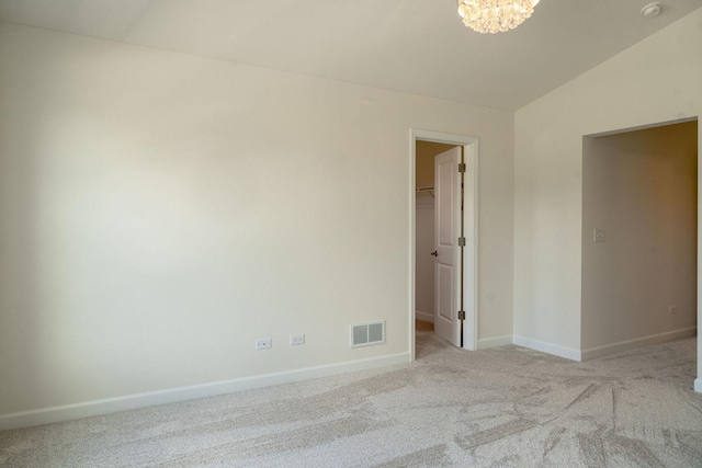 empty room featuring light carpet, vaulted ceiling, and a chandelier