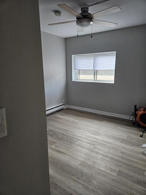 empty room with ceiling fan, a baseboard heating unit, and light wood-type flooring