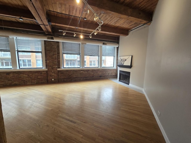 unfurnished living room featuring rail lighting, wood ceiling, beamed ceiling, brick wall, and hardwood / wood-style floors